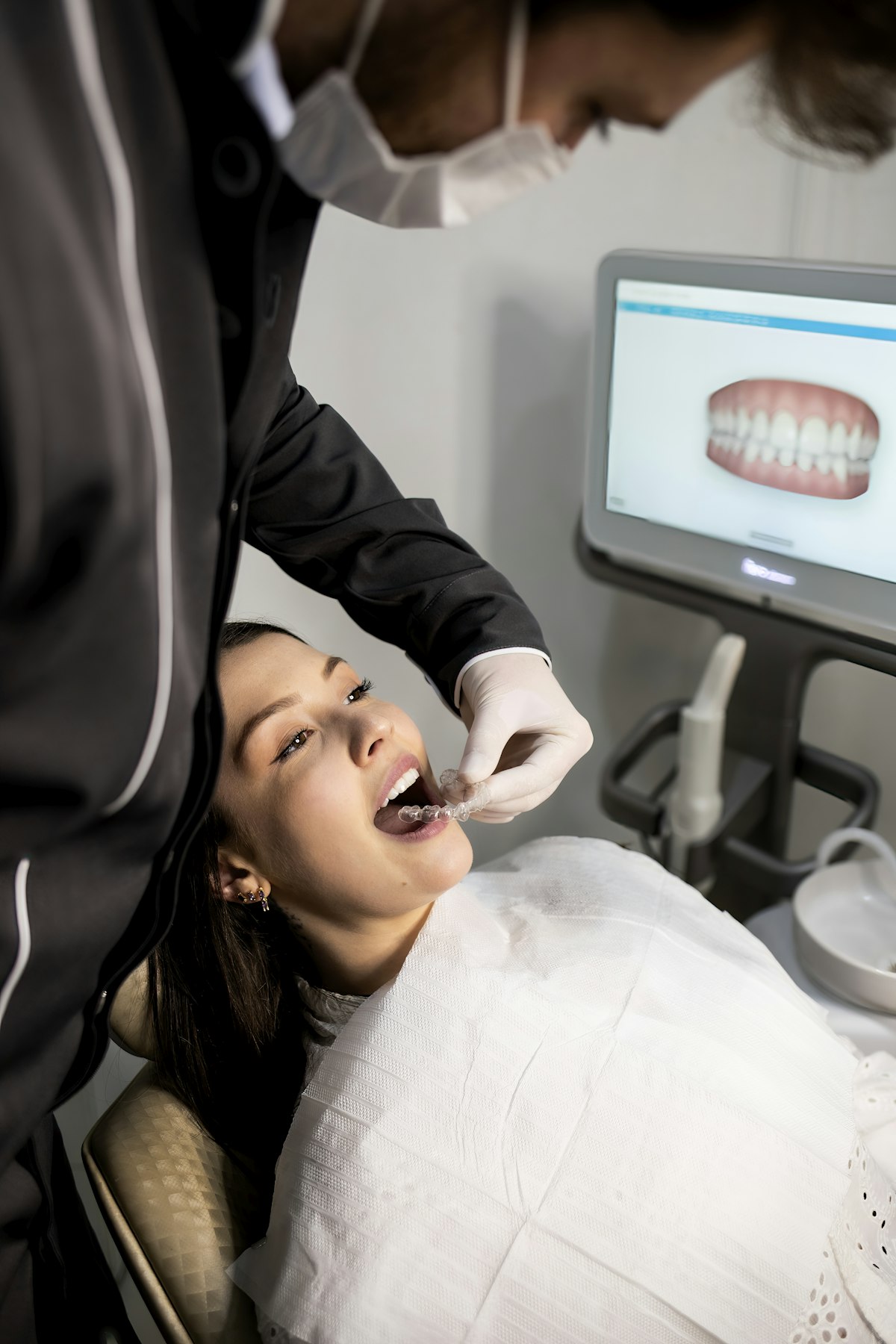Dentist fitting a clear aligner while a 3D digital scan of the patient's teeth is displayed on screen